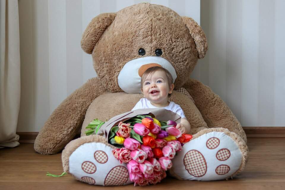 نوزاد و عروسک در کنار یک گلدان گل طبیعی