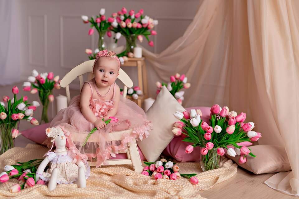 نوزاد و عروسک در کنار یک گلدان گل طبیعی