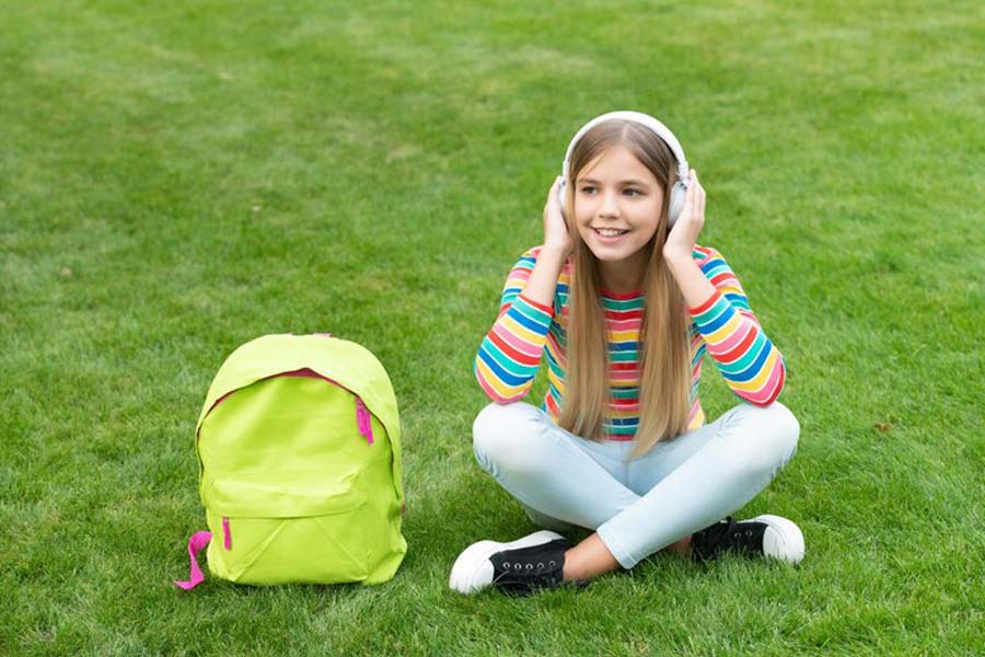 ایده عکاسی کودک در روز اول مدرسه نشسته روی چمن با کیف