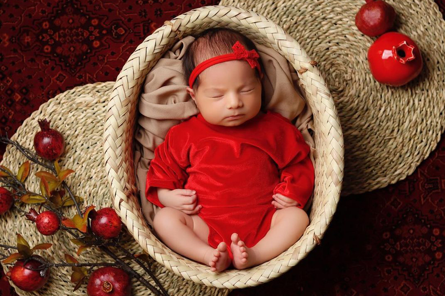 ایده‌های ژست عکس شب یلدا برای نوزاد در منزل - نوزاد داخل سبد حصیری و انارهای کوچک